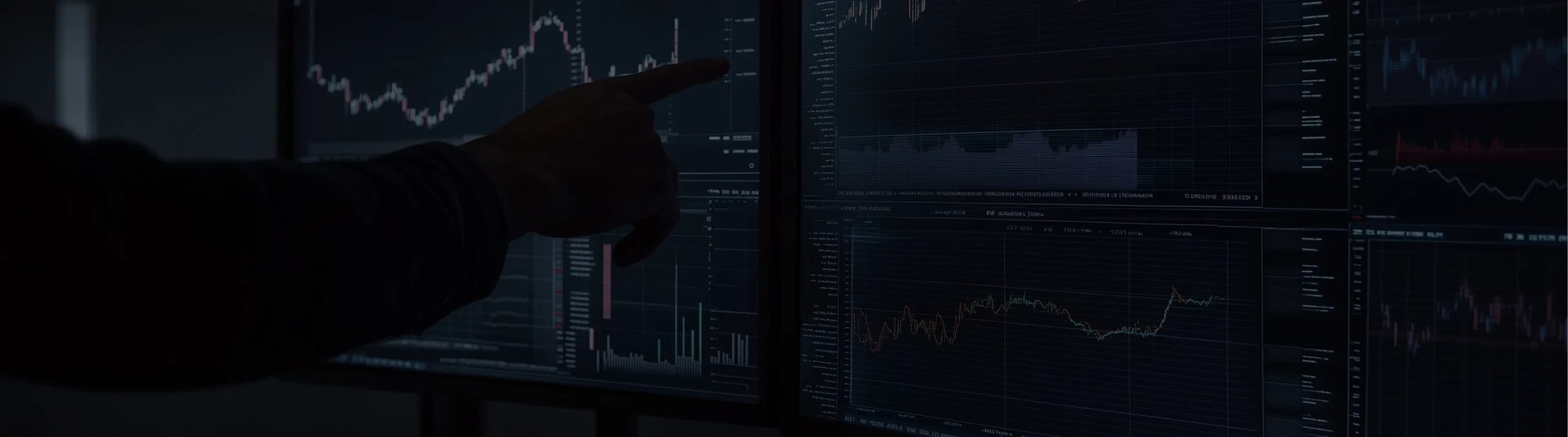 Person pointing at trading charts on multiple dark screens