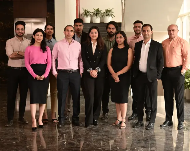 A group of 11 professionally dressed people standing indoors in a office setting.